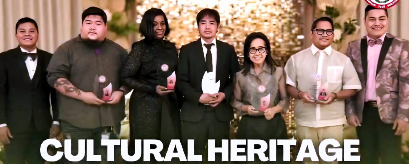 Group photo of the 2025 TEACH Cultural Heritage Awardees standing on a decorated stage, each holding an award trophy, with a warm floral and illuminated backdrop and the IAM FAME INC. logo displayed.