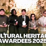 Group photo of the 2025 TEACH Cultural Heritage Awardees standing on a decorated stage, each holding an award trophy, with a warm floral and illuminated backdrop and the IAM FAME INC. logo displayed.